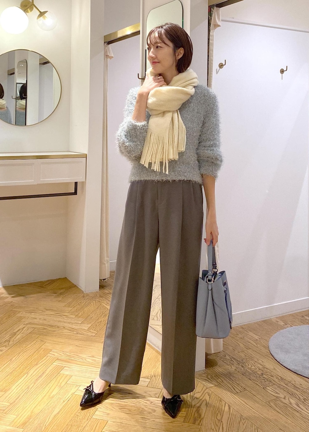 グレー系のスラックス、ブルー系のショルダーバッグ、ブラック系のパンプスを着用したレディースの冬コーディネートの2枚目の写真