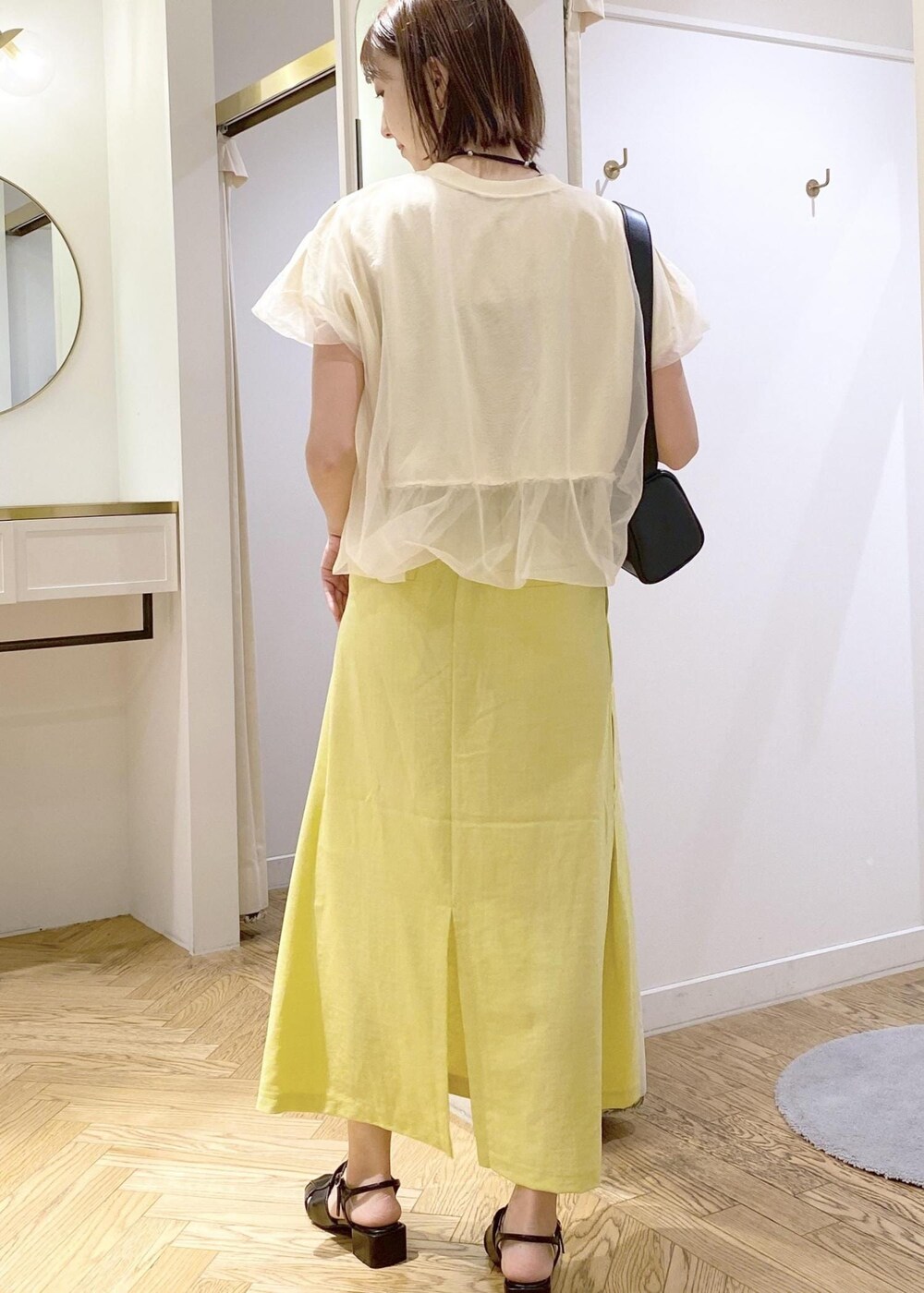 ブラック系のショルダーバッグ、ブラック系のサンダル、イエロー系のスカートを着用したレディースの春コーディネートの2枚目の写真