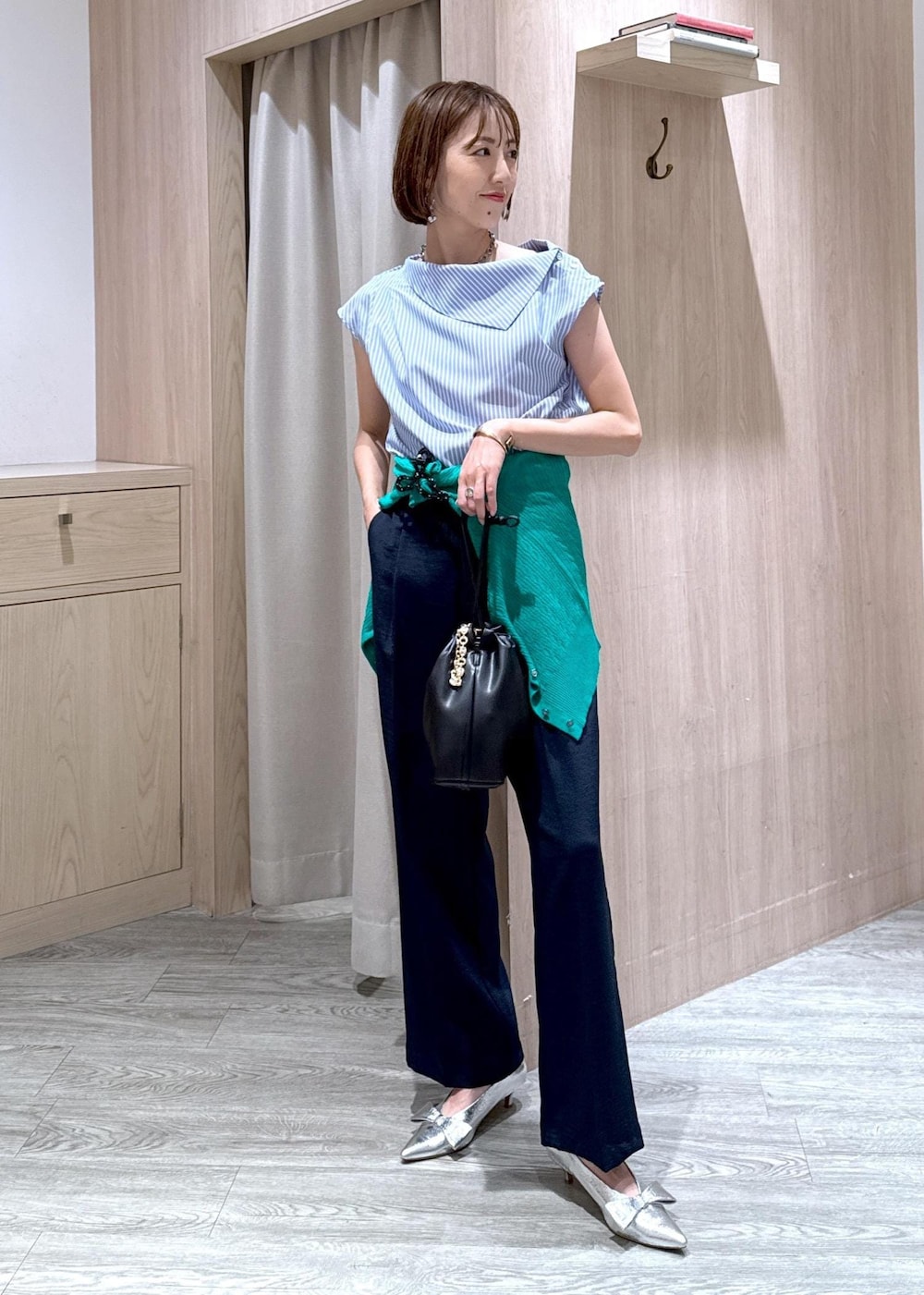 シルバー系のパンプス、ブラック系のハンドバッグ、ブルー系のスラックスを着用したレディースの夏コーディネートの2枚目の写真