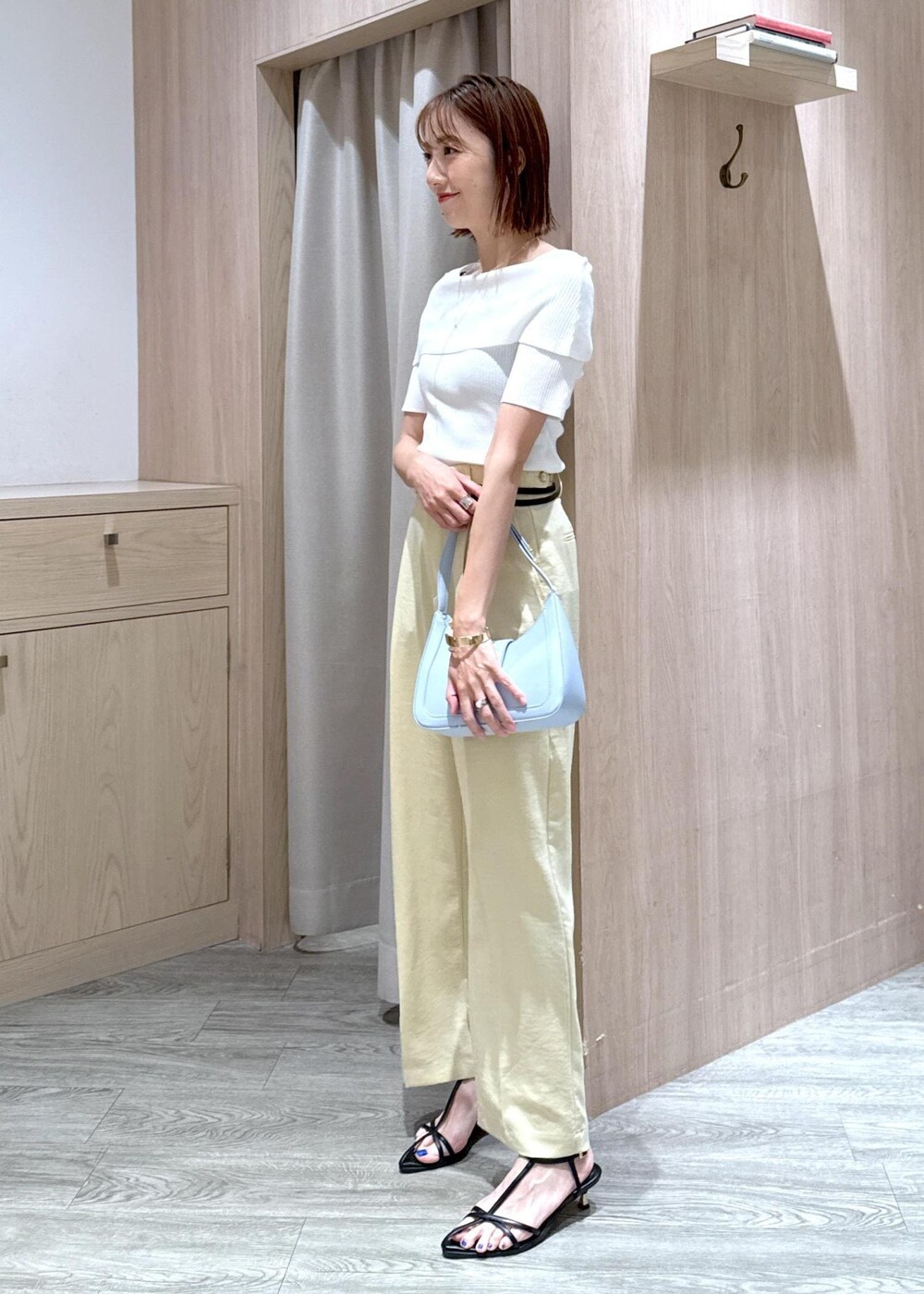 ブルー系のハンドバッグ、ブラック系のサンダル、イエロー系のスラックスを着用したレディースの夏コーディネートの2枚目の写真