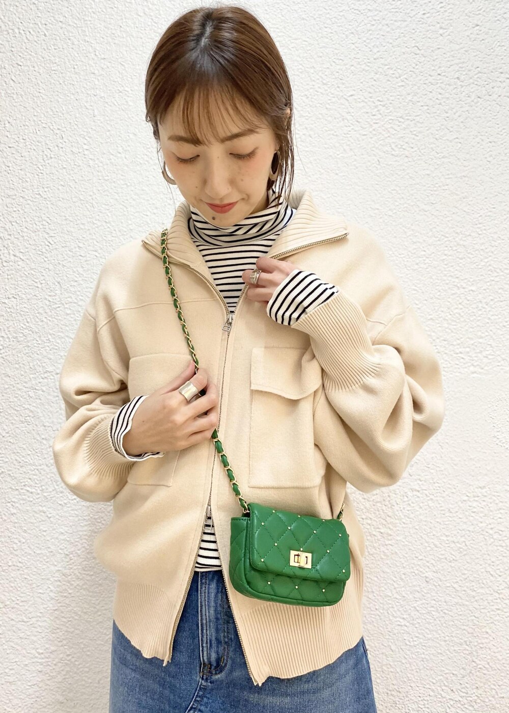 グリーン系のショルダーバッグ、ホワイト系のニット/セーター、ブルー系のデニムスカートを着用したレディースの冬コーディネートの4枚目の写真