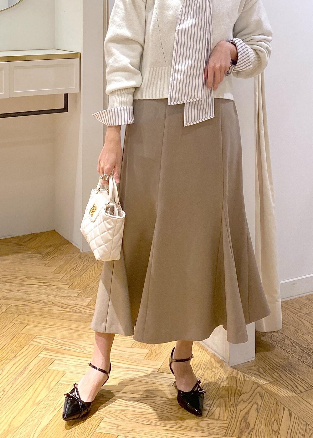 ブラック系のパンプス、ベージュ系のスカート、ホワイト系のシャツ/ブラウスを着用したレディースの冬コーディネートの5枚目の写真