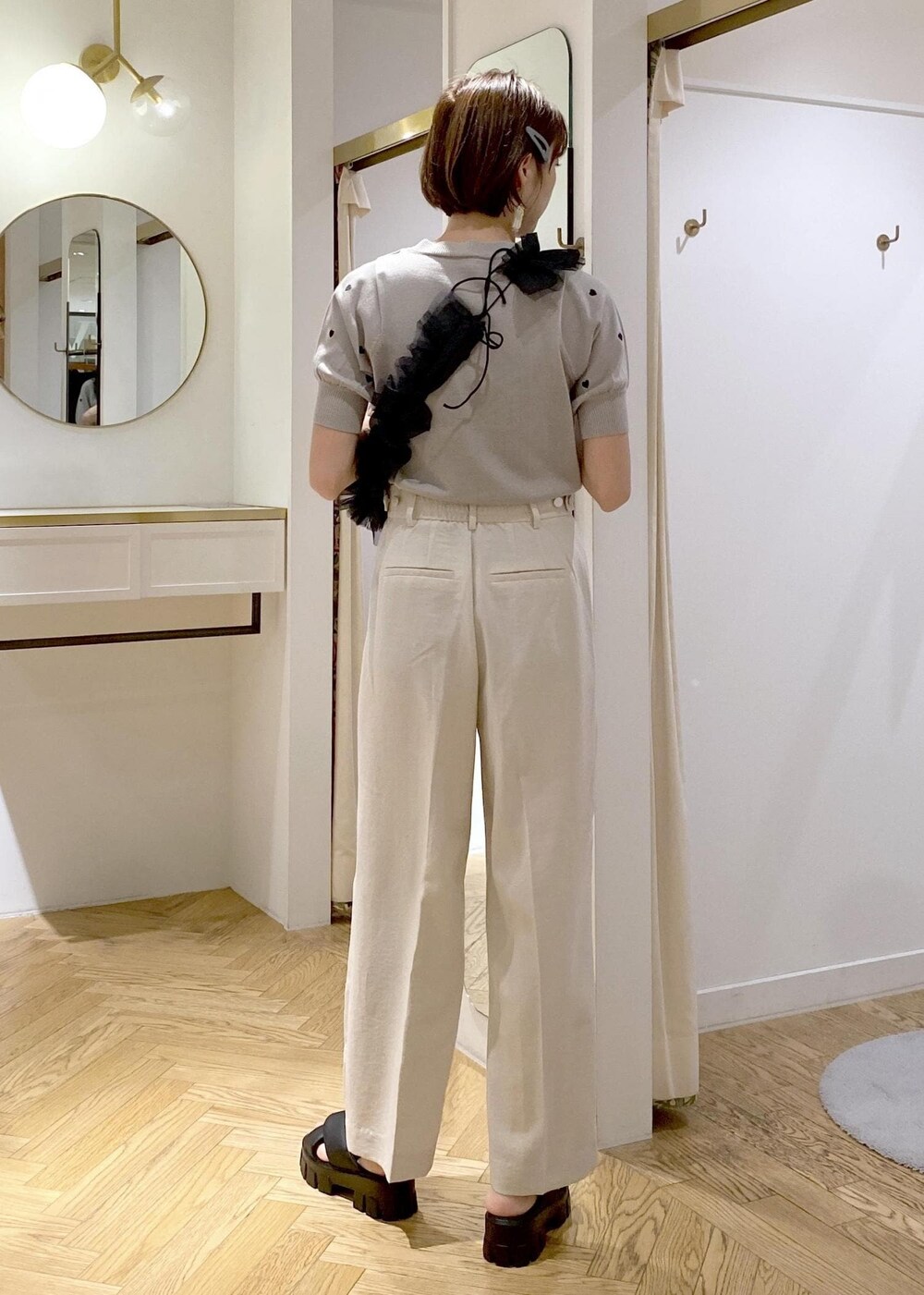 ブラック系のショルダーバッグ、グレー系のニット/セーター、ホワイト系のスラックスを着用したレディースの夏コーディネートの2枚目の写真