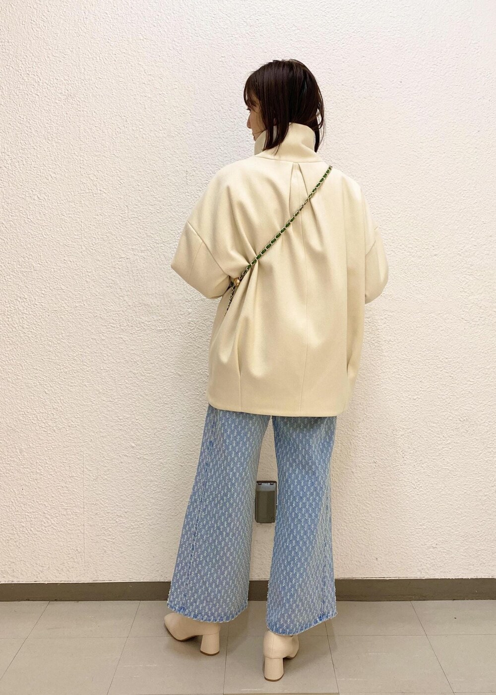 ホワイト系のステンカラーコート、グリーン系のショルダーバッグ、ホワイト系のニット/セーターを着用したレディースの冬コーディネートの2枚目の写真