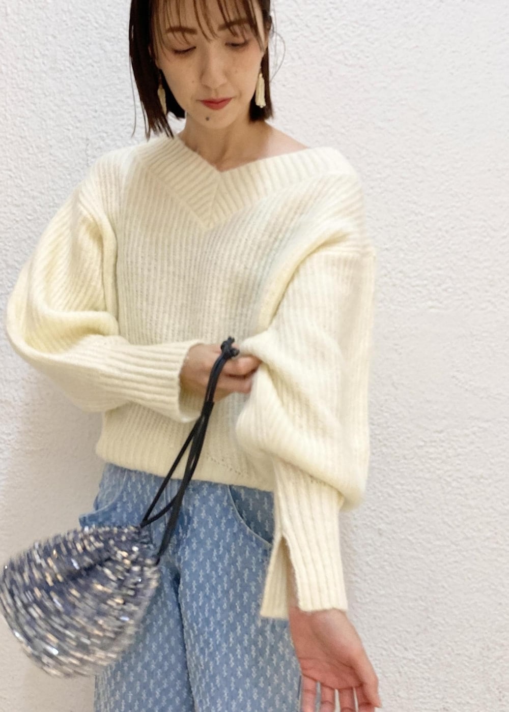 シルバー系のハンドバッグ、ホワイト系のニット/セーター、ブルー系のデニムパンツを着用したレディースの冬コーディネートの4枚目の写真