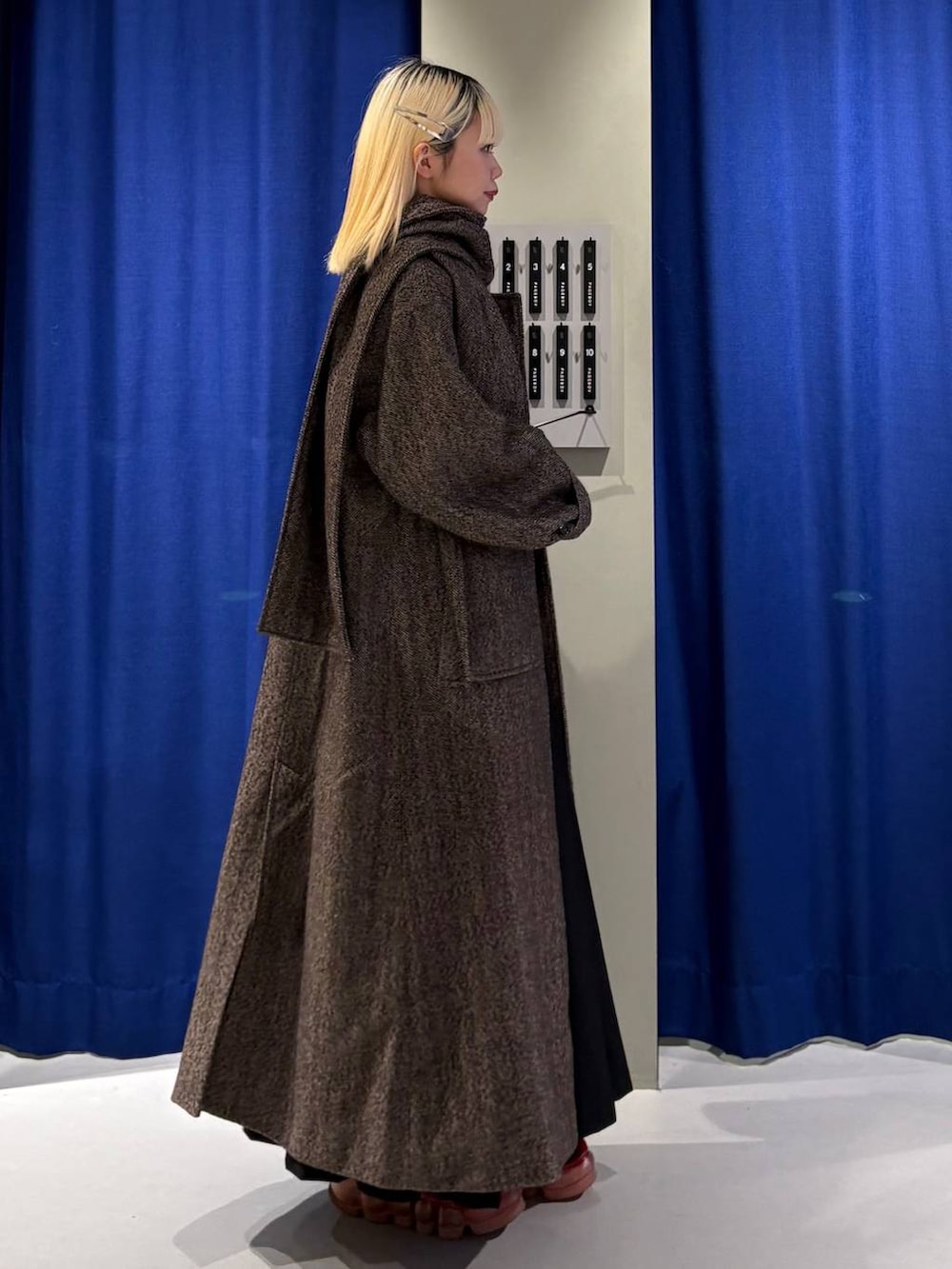 ブラウン系のチェスターコート、ブラック系のスカート、レッド系のニット/セーターを着用したレディースの冬コーディネートの2枚目の写真