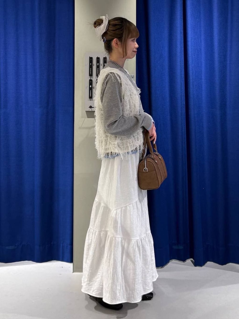 ブラウン系のボストンバッグ、ブラック系のスニーカー、ホワイト系のベストを着用したレディースの冬コーディネートの2枚目の写真