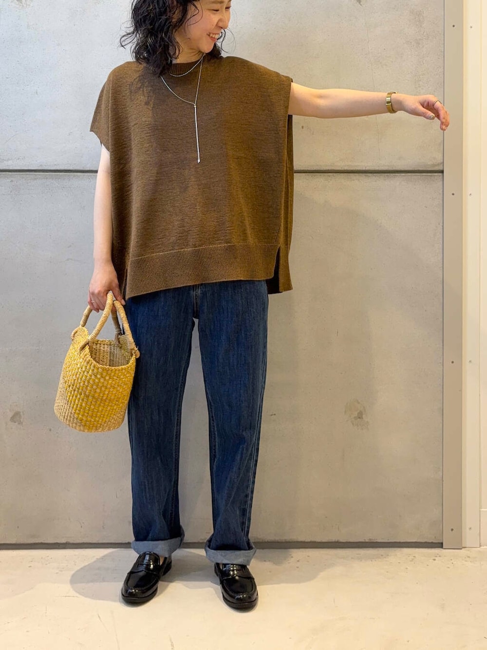 イエロー系のショルダーバッグ、ブルー系のデニムパンツ、ブラウン系のニット/セーターを着用したレディースの夏コーディネートの2枚目の写真