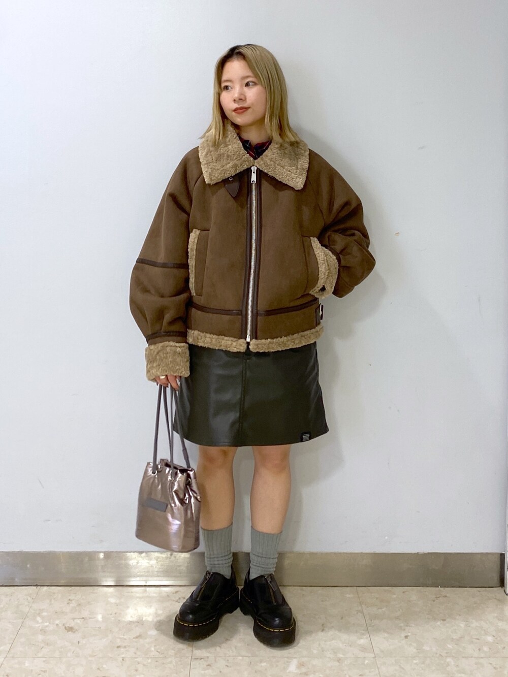 ブラウン系のムートンコート、シルバー系のショルダーバッグ、グリーン系のジャンパースカートを着用したレディースの冬コーディネートの2枚目の写真