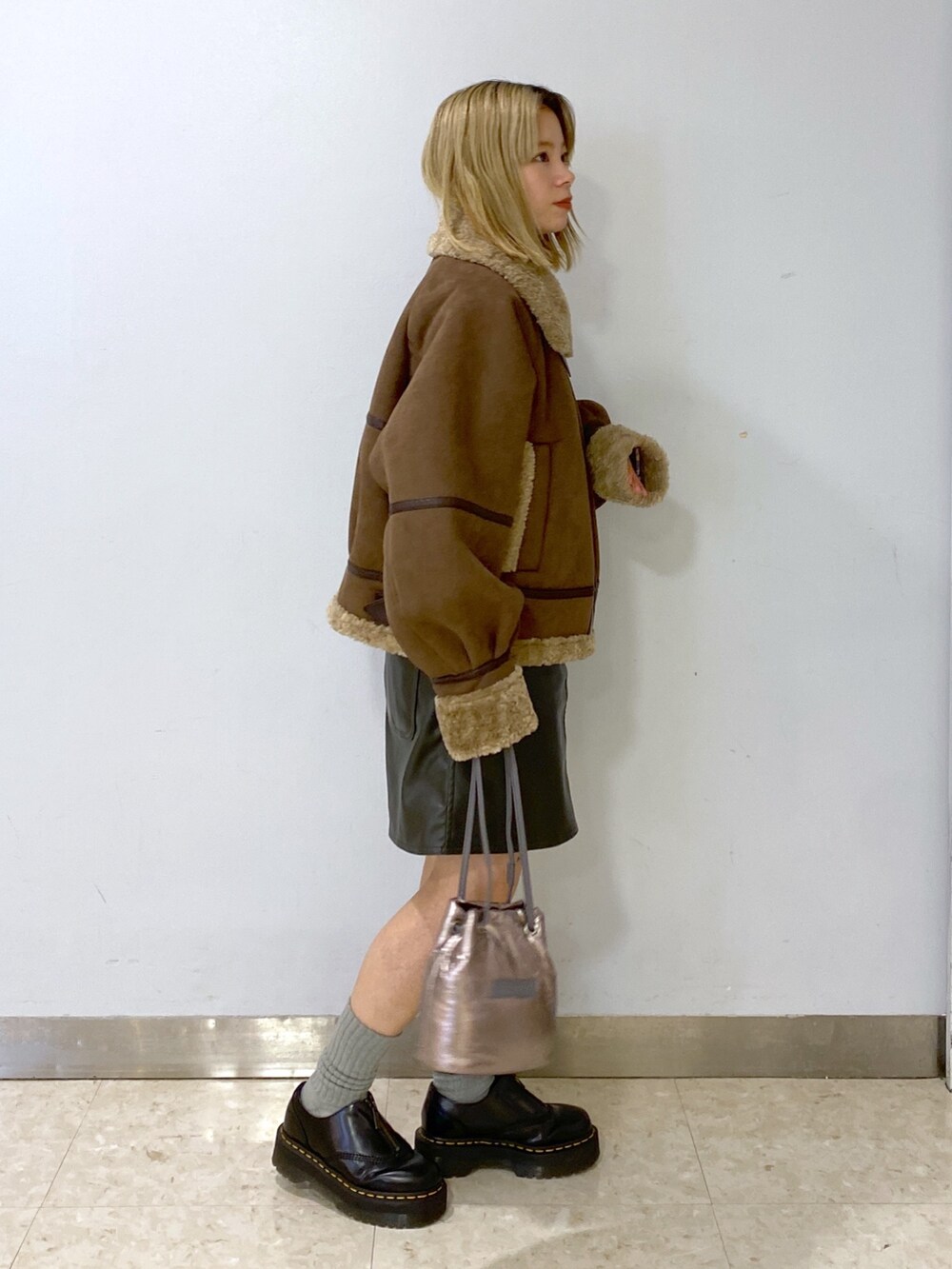 ブラウン系のムートンコート、シルバー系のショルダーバッグ、グリーン系のジャンパースカートを着用したレディースの冬コーディネートの5枚目の写真
