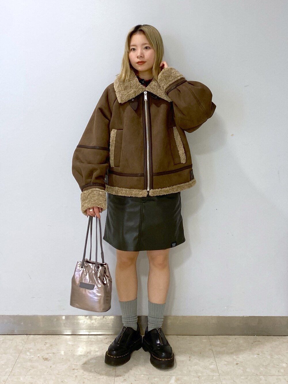 ブラウン系のムートンコート、シルバー系のショルダーバッグ、グリーン系のジャンパースカートを着用したレディースの冬コーディネートの3枚目の写真
