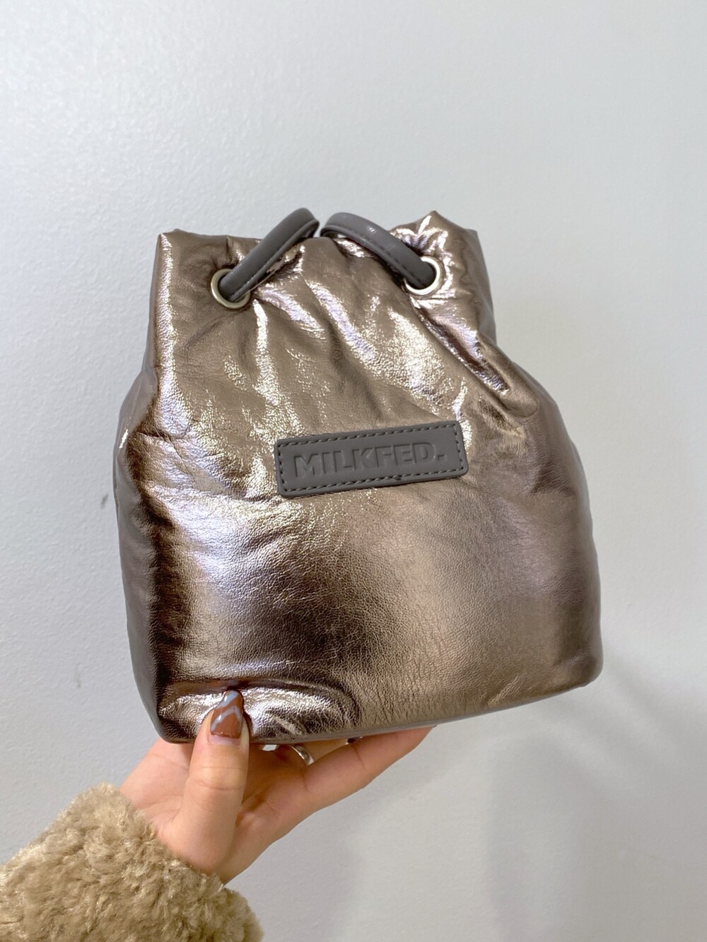 ブラウン系のムートンコート、シルバー系のショルダーバッグ、グリーン系のジャンパースカートを着用したレディースの冬コーディネートの7枚目の写真