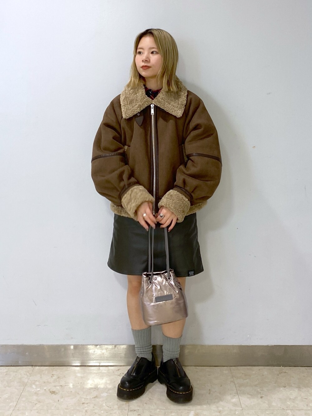 ブラウン系のムートンコート、シルバー系のショルダーバッグ、グリーン系のジャンパースカートを着用したレディースの冬コーディネートの4枚目の写真