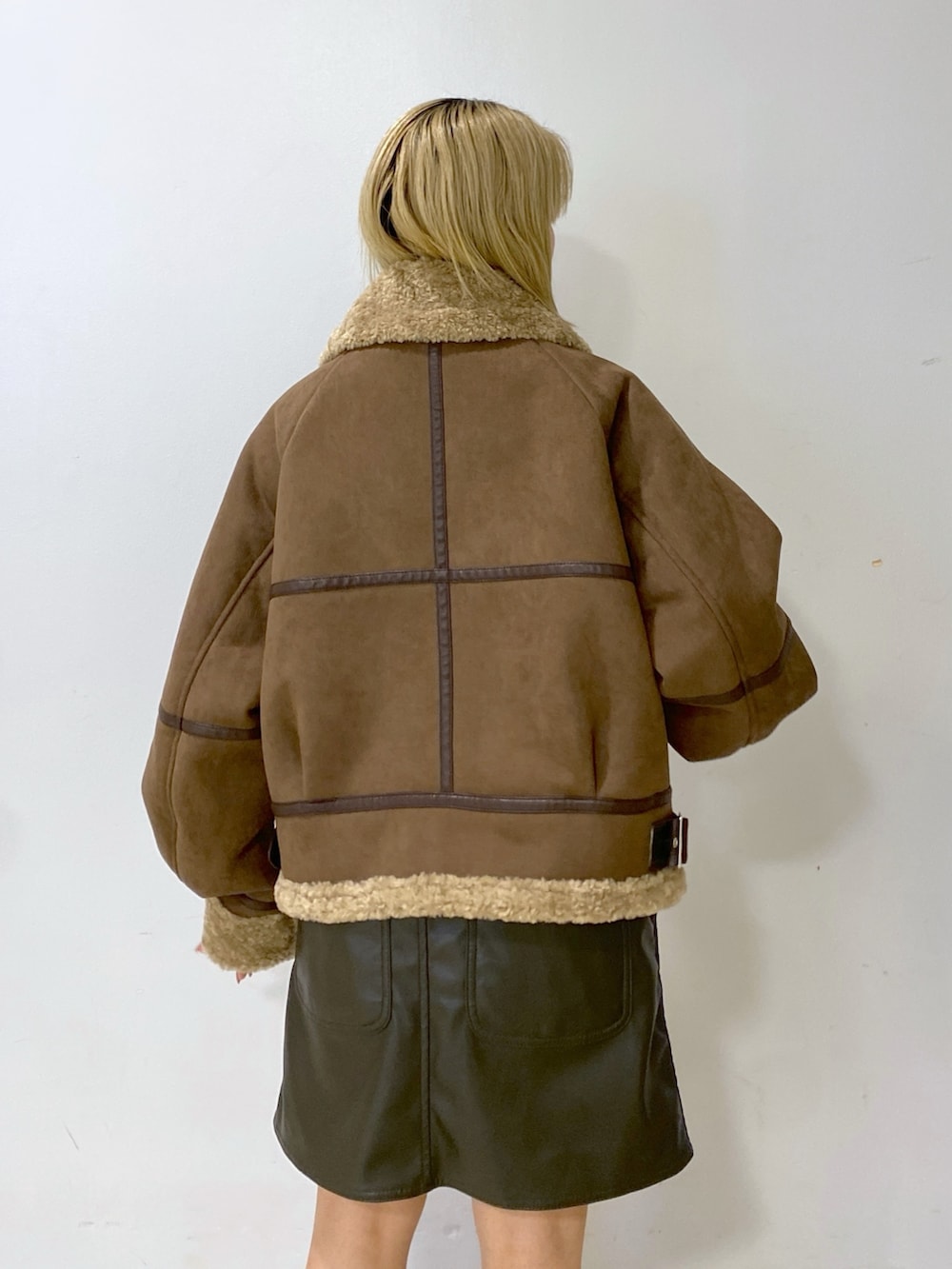 ブラウン系のムートンコート、シルバー系のショルダーバッグ、グリーン系のジャンパースカートを着用したレディースの冬コーディネートの9枚目の写真