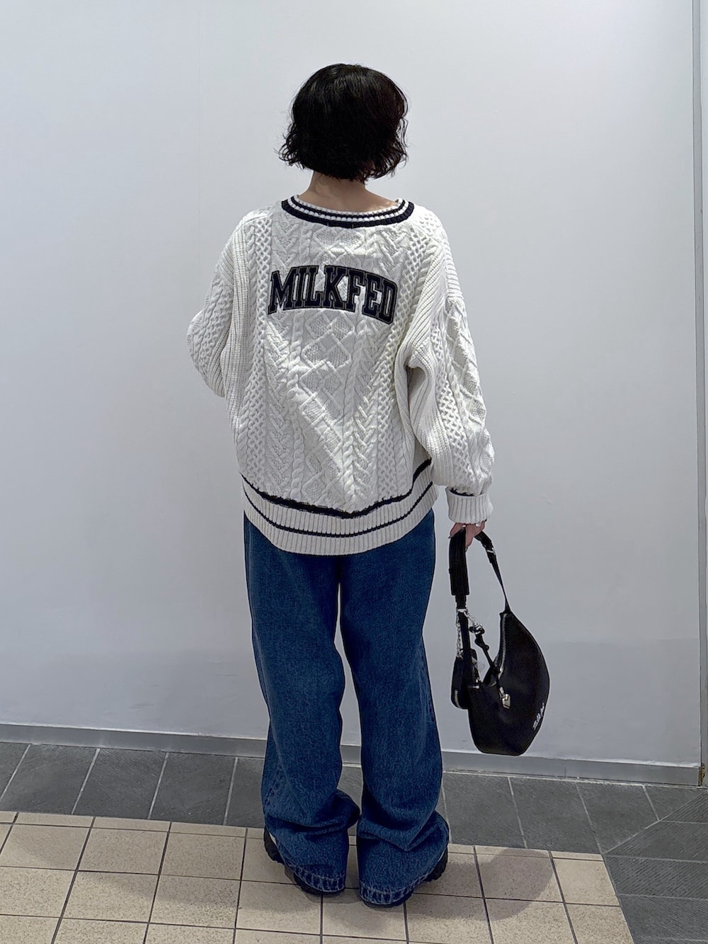 ブルー系のデニムパンツ、ホワイト系のニット/セーター、ブラック系のハンドバッグを着用したレディースの秋コーディネートの5枚目の写真