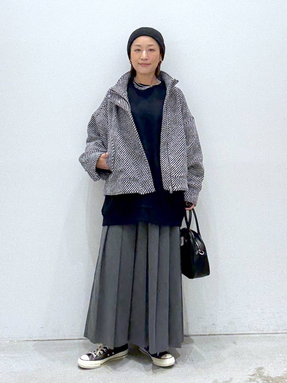 グレー系のスカート、ブラウン系のスニーカー、ブラック系のボストンバッグを着用したレディースの秋コーディネートの2枚目の写真