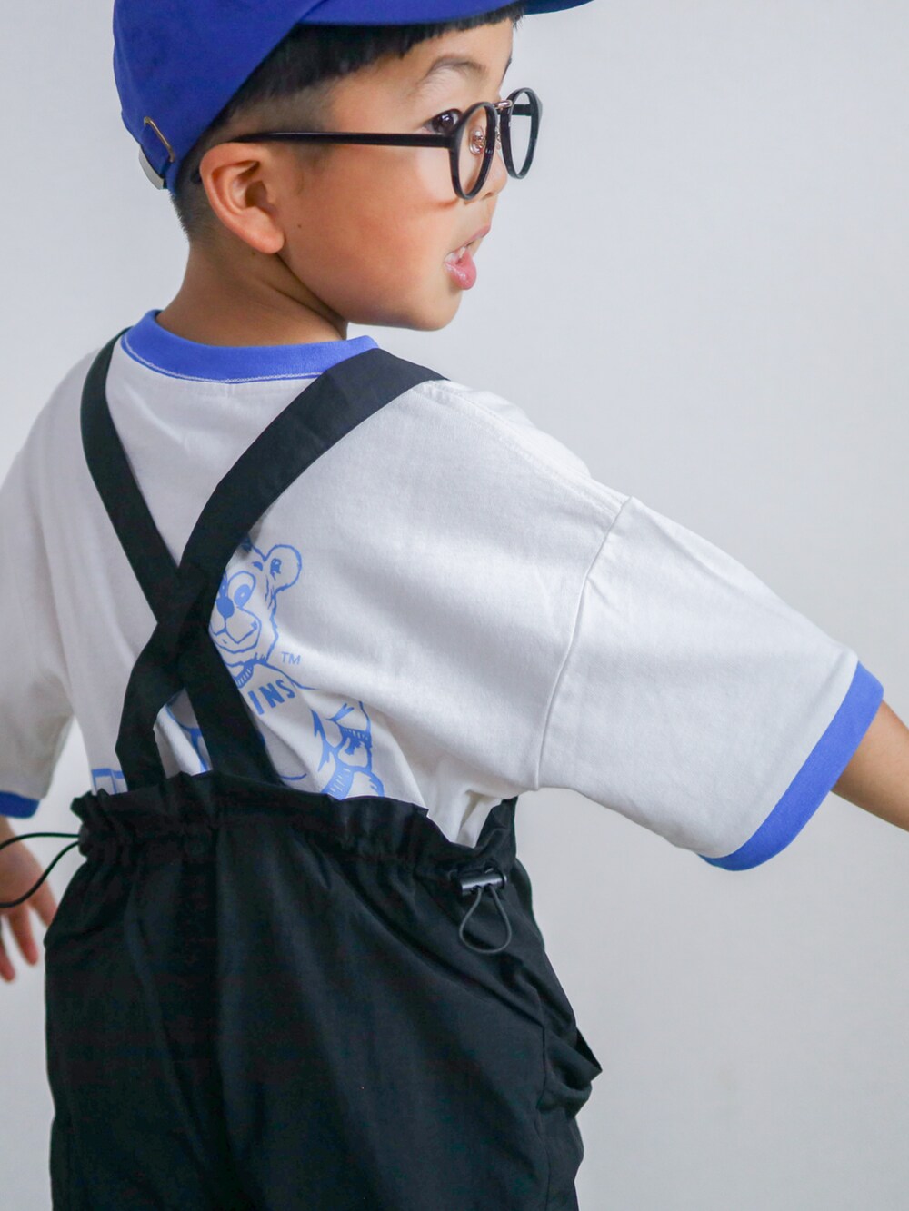 ブルー系のTシャツ/カットソー、ホワイト系のスニーカー、ブラック系のサロペット/オーバーオールを着用したキッズの夏コーディネートの3枚目の写真