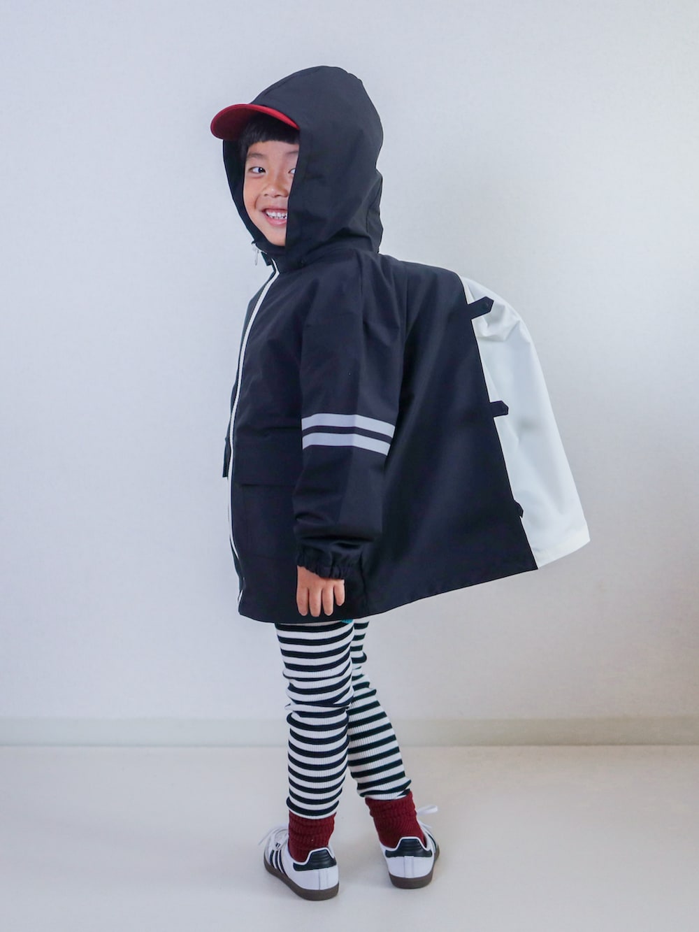 ブラック系のナイロンジャケット、ホワイト系のスニーカー、レッド系のキャップを着用したキッズの秋コーディネートの2枚目の写真