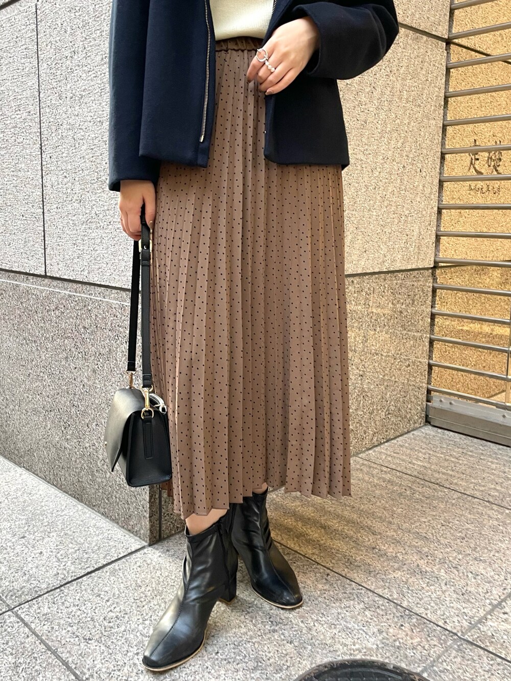 ブラウン系のスカート、ブラック系のショルダーバッグ、ブラック系のブーツを着用したレディースの秋コーディネートの5枚目の写真