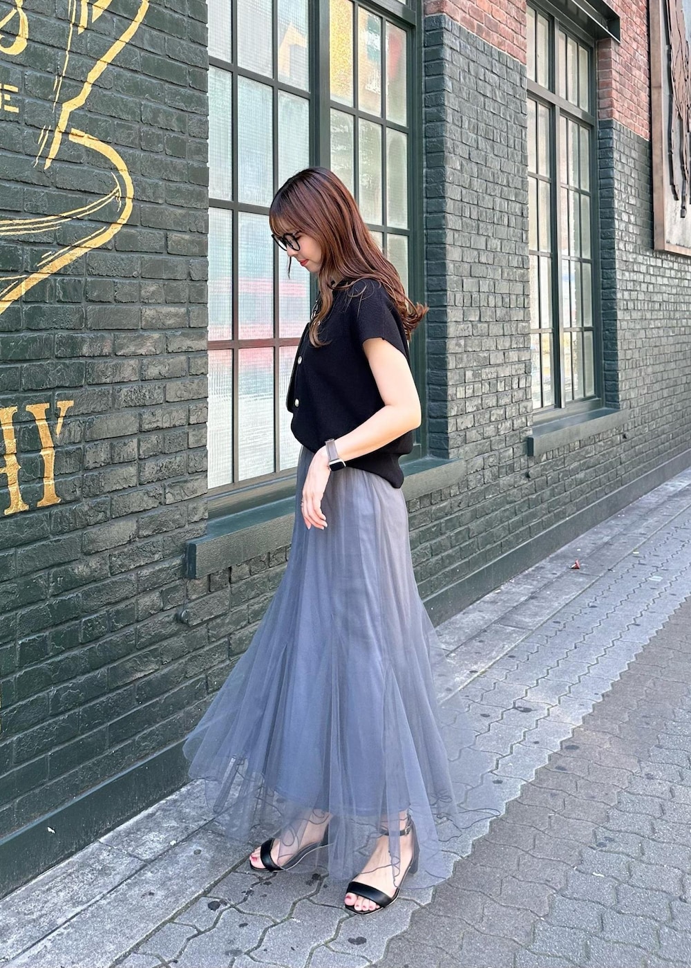 グレー系のスカート、ブラック系のニット/セーター、ブラック系のショルダーバッグを着用したレディースの春コーディネートの4枚目の写真