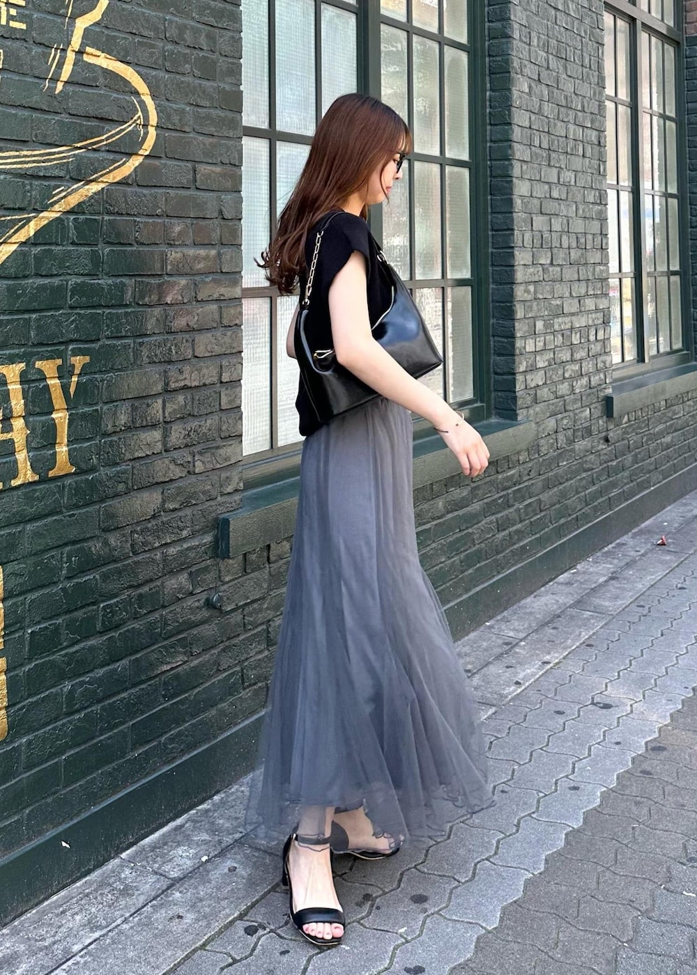 グレー系のスカート、ブラック系のニット/セーター、ブラック系のショルダーバッグを着用したレディースの春コーディネートの3枚目の写真