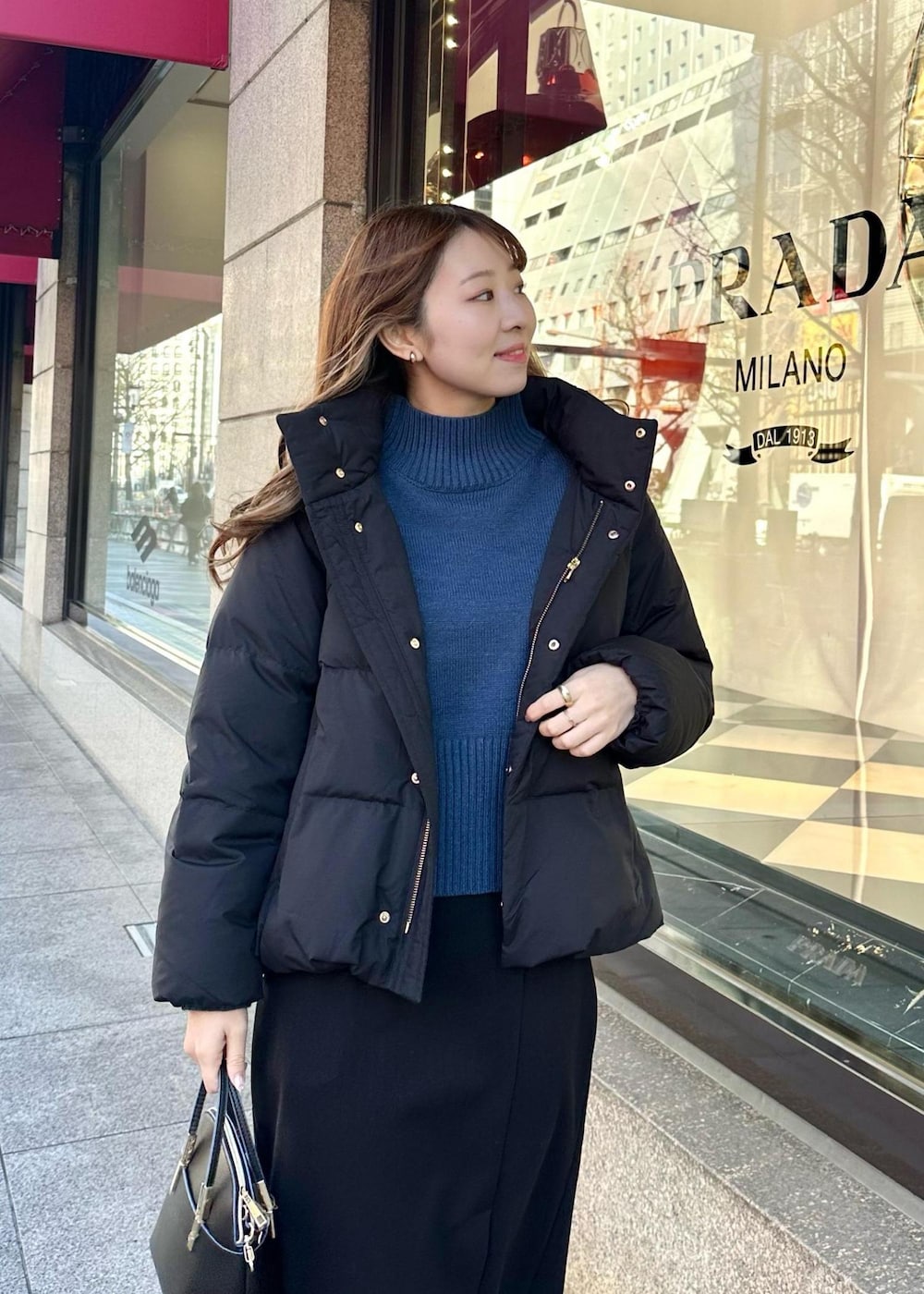 ブルー系のニット/セーター、ブラック系のダウンジャケット/コート、ブラック系のショルダーバッグを着用したレディースの冬コーディネートの4枚目の写真