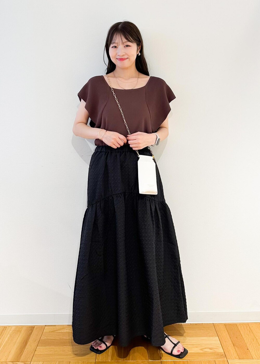 ホワイト系のショルダーバッグ、ブラウン系のニット/セーター、ブラック系のスカートを着用したレディースの夏コーディネートの2枚目の写真