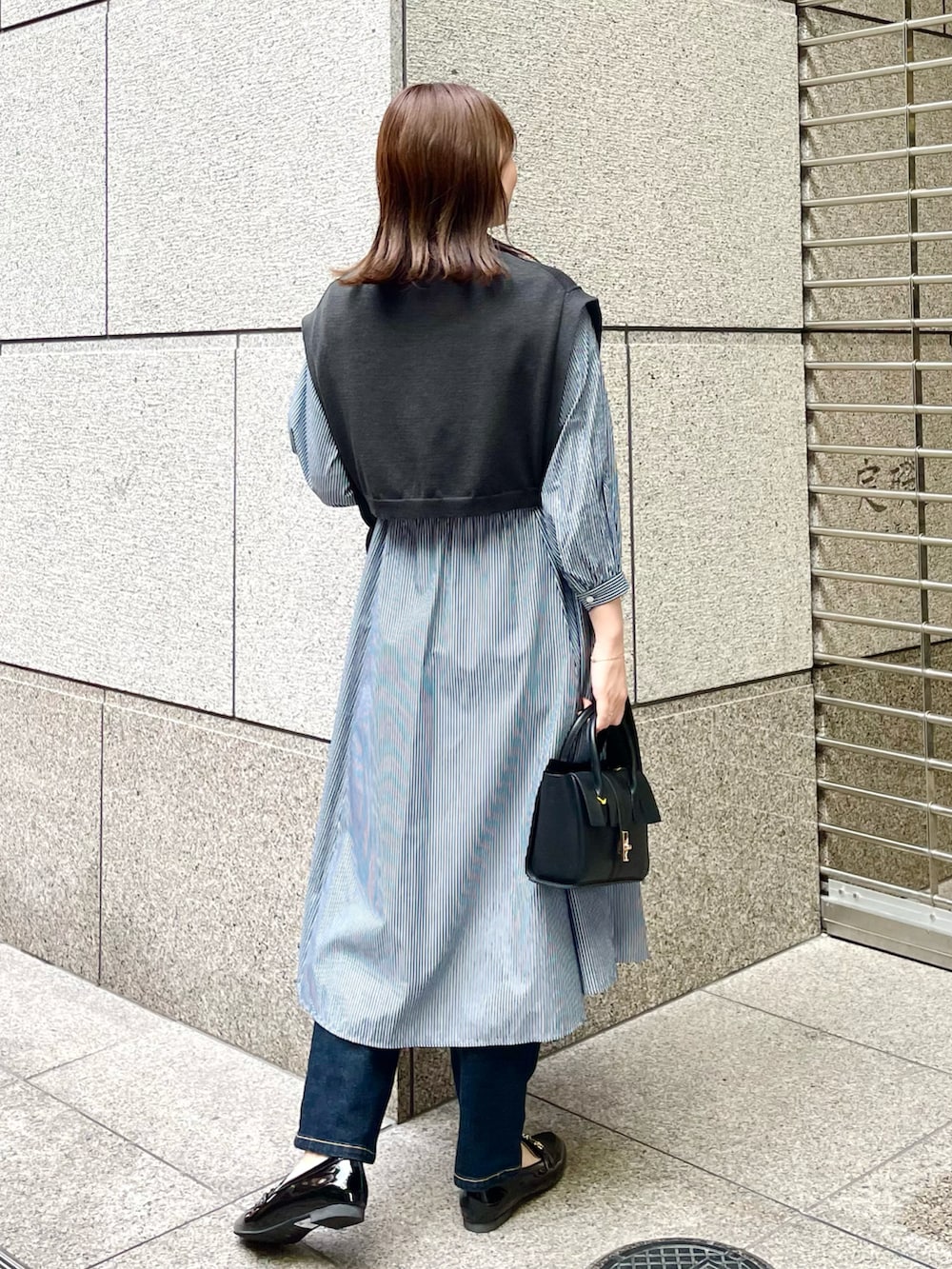 ブラック系のベスト、ブルー系のワンピース、ブラック系のショルダーバッグを着用したレディースの春コーディネートの2枚目の写真