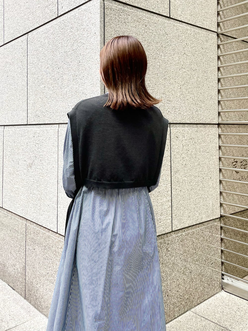 ブラック系のベスト、ブルー系のワンピース、ブラック系のショルダーバッグを着用したレディースの春コーディネートの4枚目の写真