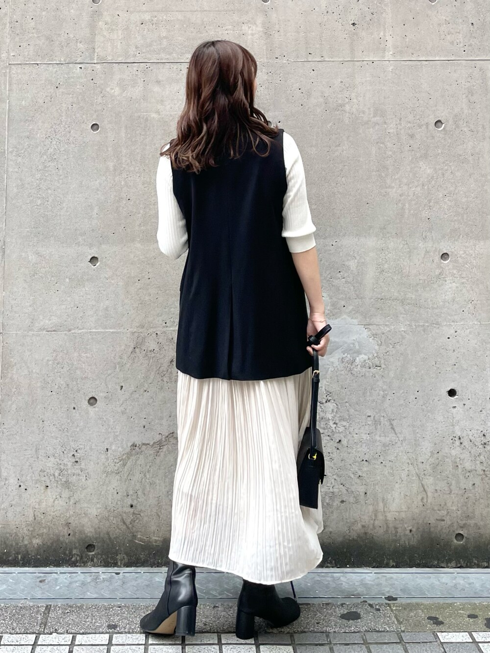 ブラック系のショルダーバッグ、ブラック系のベスト、ホワイト系のニット/セーターを着用したレディースの秋コーディネートの2枚目の写真