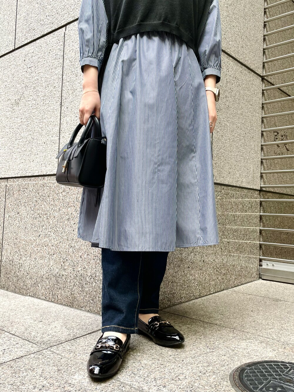 ブラック系のベスト、ブルー系のワンピース、ブラック系のショルダーバッグを着用したレディースの春コーディネートの5枚目の写真