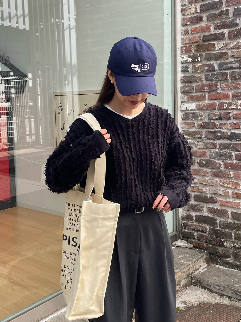 ホワイト系のトートバッグ、ブラック系のニット/セーター、ホワイト系のスニーカーを着用したレディースの春コーディネートの2枚目の写真