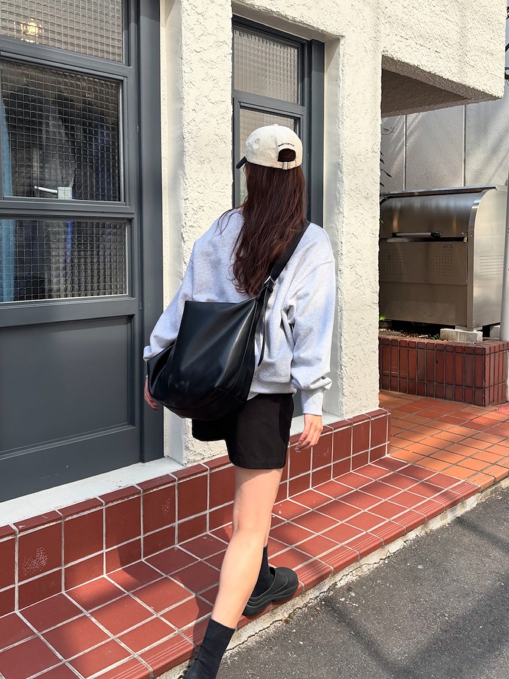グレー系のスウェット、ブラック系のショルダーバッグ、ブラック系のレインシューズを着用したレディースの春コーディネートの4枚目の写真