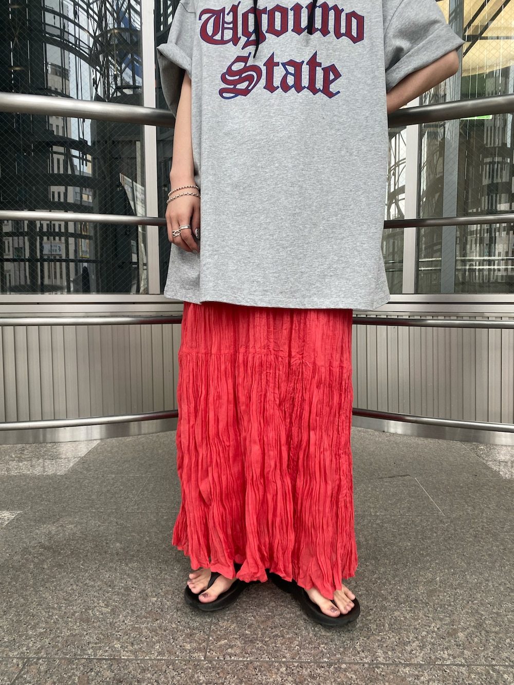 レッド系のスカート、グレー系のTシャツ/カットソー、ブラック系のハットを着用したレディースの夏コーディネートの3枚目の写真