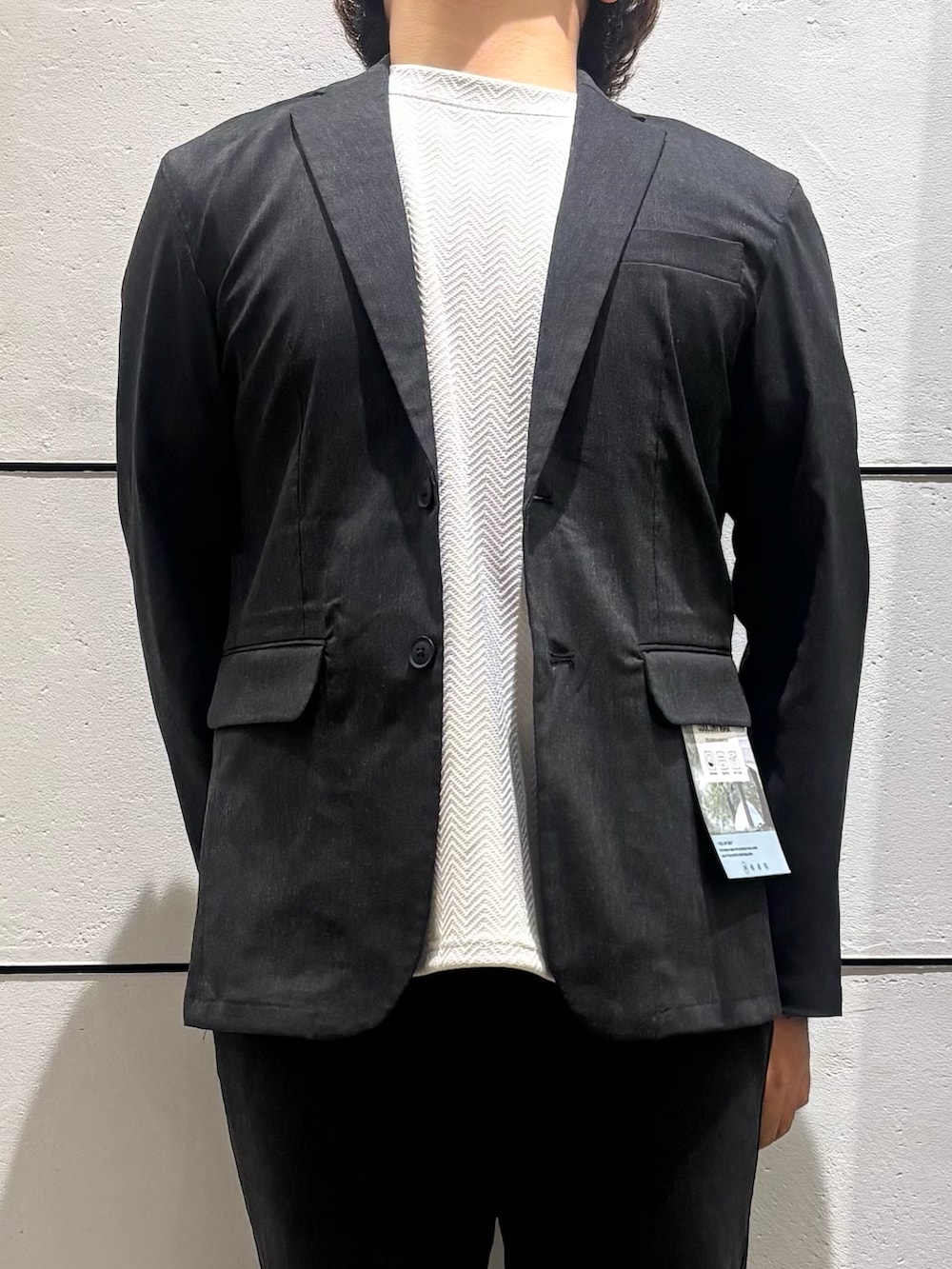 ブラック系のテーラードジャケット、ベージュ系のTシャツ/カットソー、ブラック系のスラックスを着用したメンズの春コーディネートの4枚目の写真