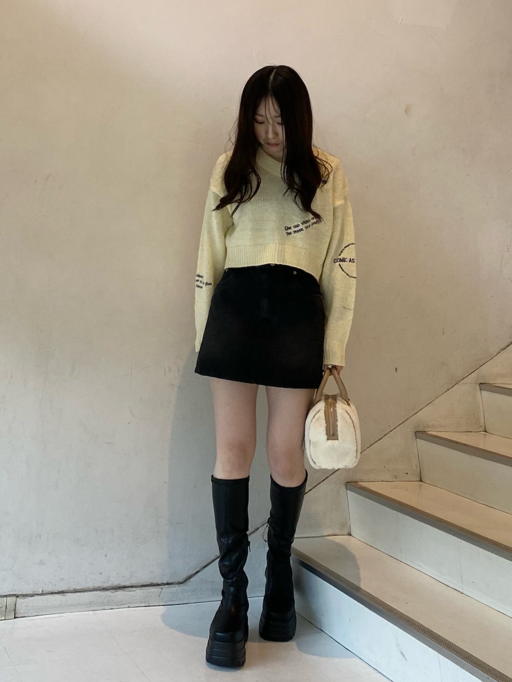 ブラック系のブーツ、ブラック系のデニムスカート、ホワイト系のボストンバッグを着用したレディースの冬コーディネートの4枚目の写真