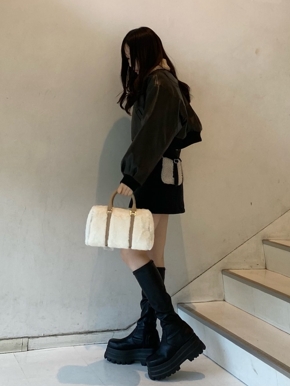 ブラック系のブーツ、ブラック系のデニムスカート、ホワイト系のボストンバッグを着用したレディースの冬コーディネートの2枚目の写真
