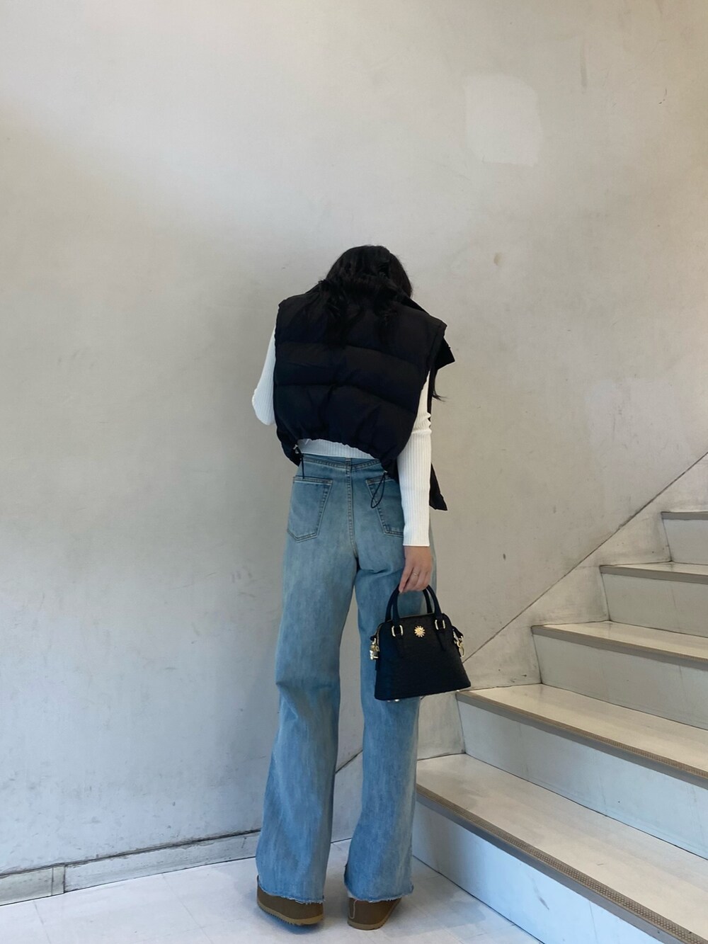 ブラック系のダウンベスト、ブルー系のデニムパンツ、ベージュ系のスリッポンを着用したレディースの秋コーディネートの2枚目の写真