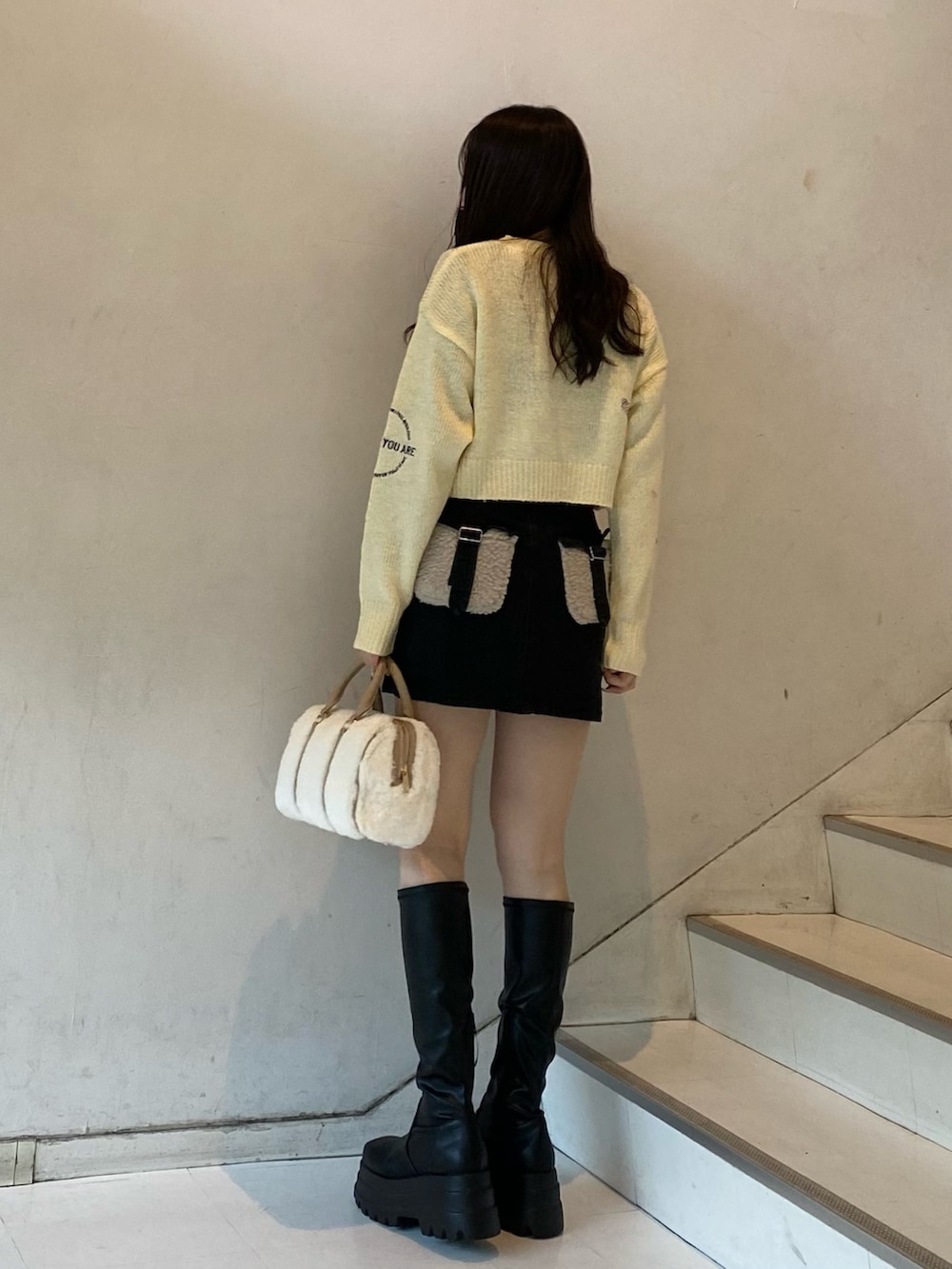 ブラック系のブーツ、ブラック系のデニムスカート、ホワイト系のボストンバッグを着用したレディースの冬コーディネートの5枚目の写真