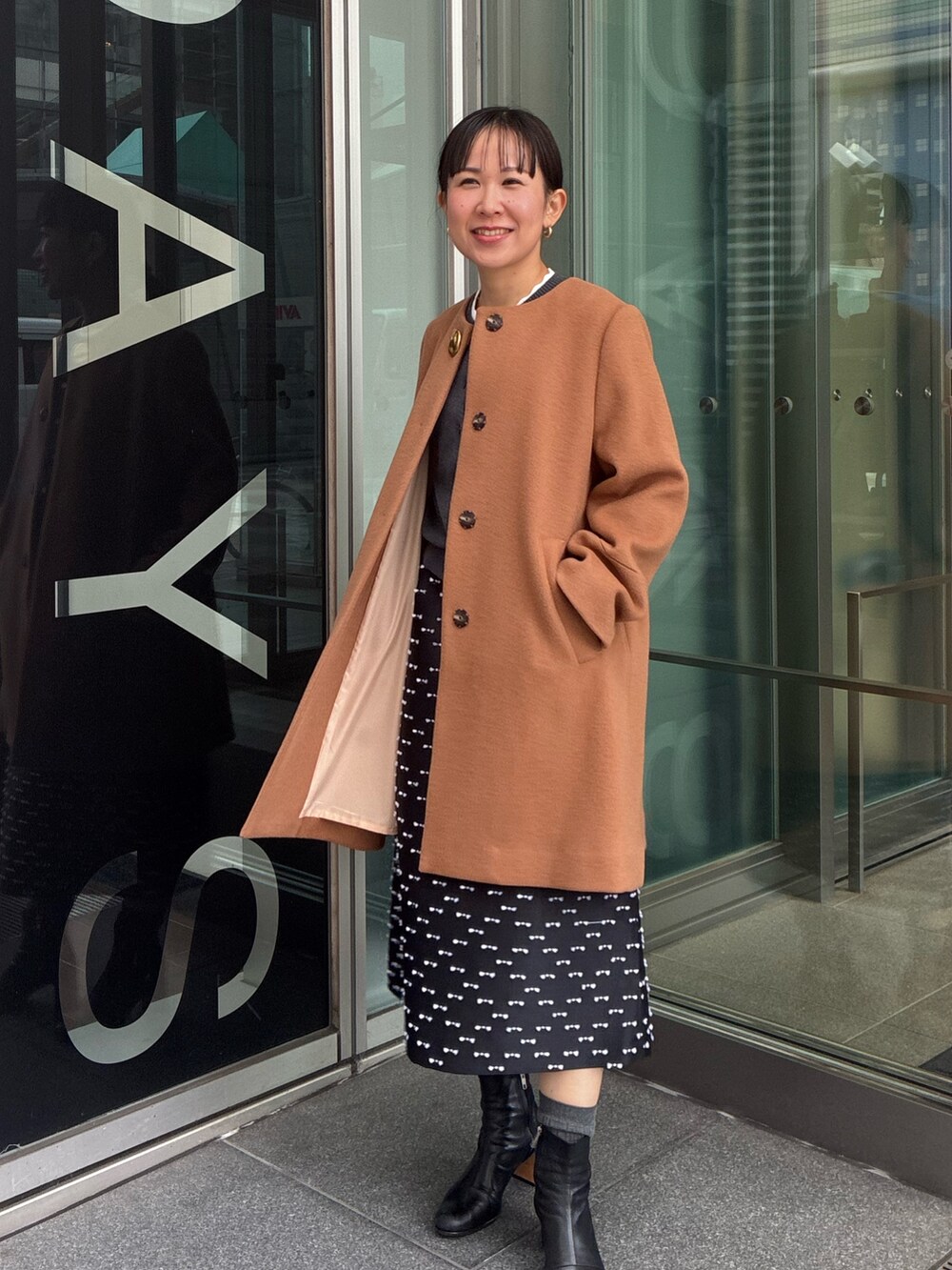 イエロー系のノーカラーコート、グレー系のカーディガン/ボレロ、ブラック系のスカートを着用したレディースの冬コーディネートの2枚目の写真