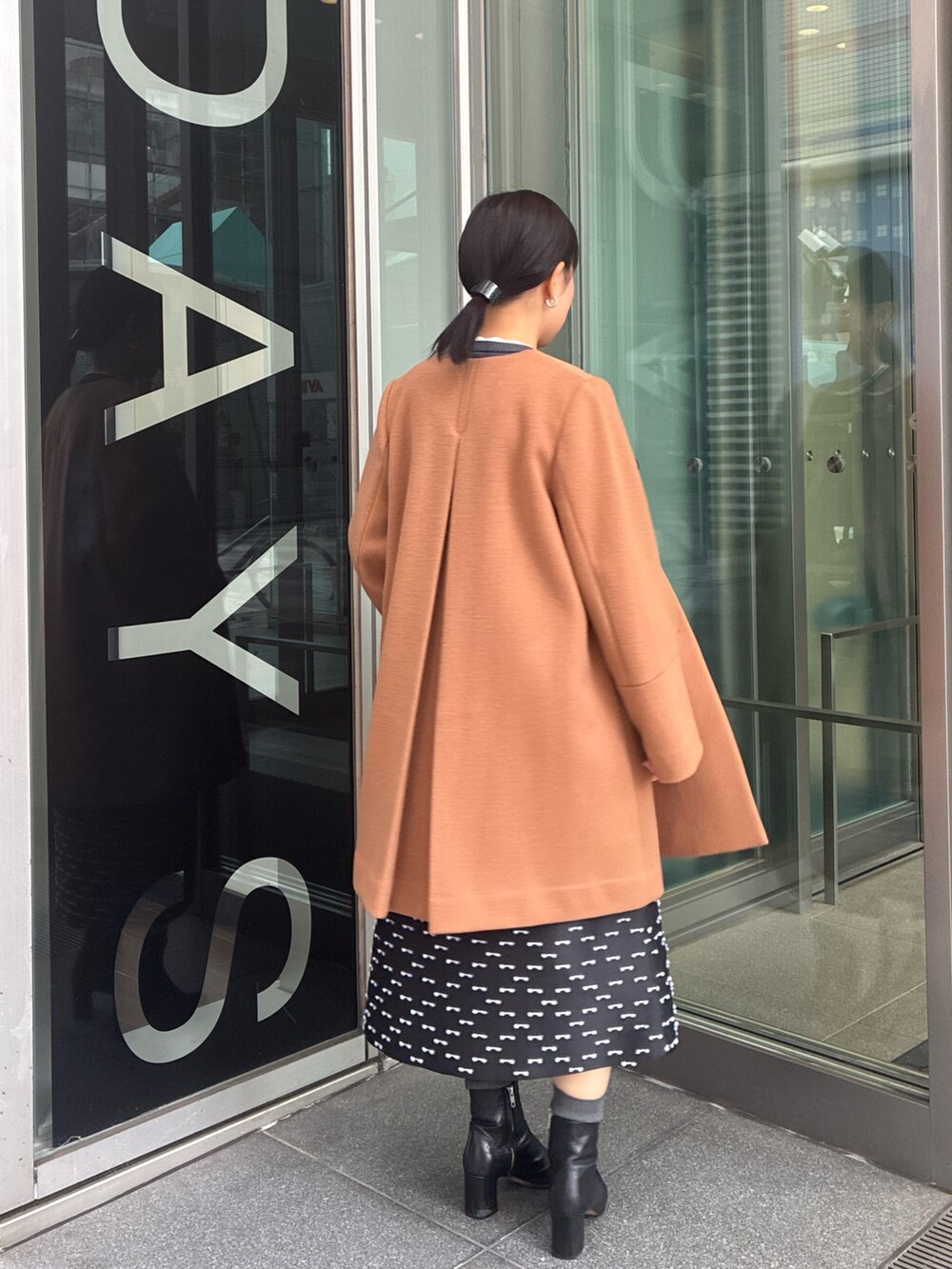 イエロー系のノーカラーコート、グレー系のカーディガン/ボレロ、ブラック系のスカートを着用したレディースの冬コーディネートの3枚目の写真