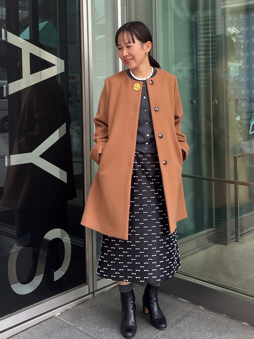 イエロー系のノーカラーコート、グレー系のカーディガン/ボレロ、ブラック系のスカートを着用したレディースの冬コーディネートの4枚目の写真