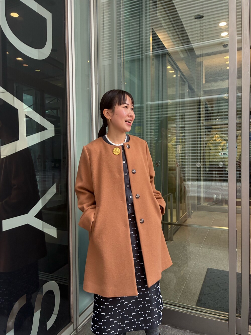 イエロー系のノーカラーコート、グレー系のカーディガン/ボレロ、ブラック系のスカートを着用したレディースの冬コーディネートの5枚目の写真