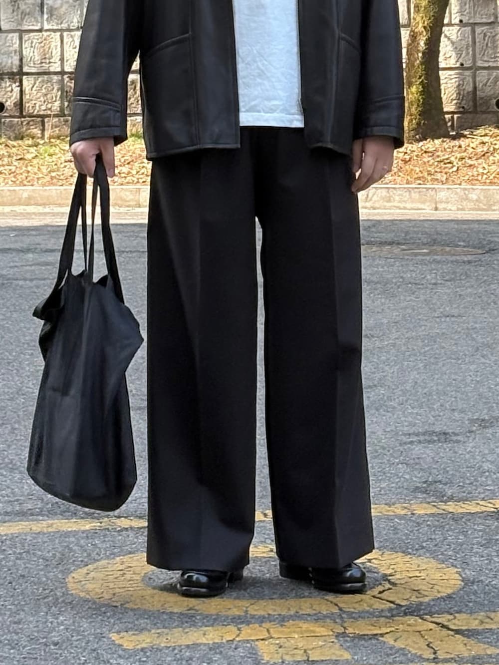 ブラック系のスラックス、ブラック系のドレスシューズ、ブラック系のトートバッグを着用したメンズの春コーディネートの3枚目の写真