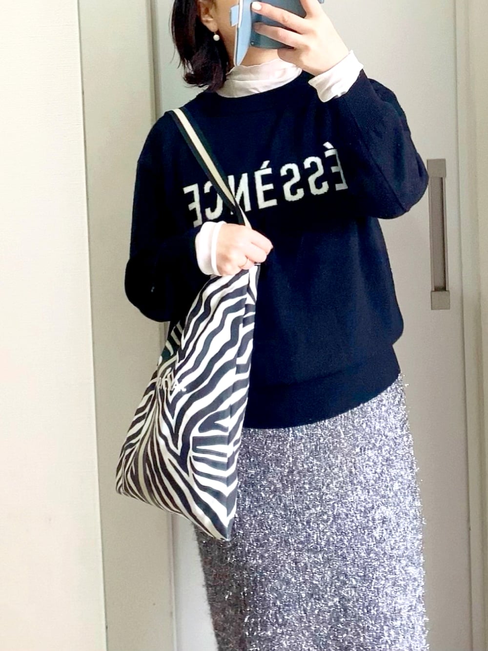 ホワイト系のTシャツ/カットソー、ブラック系のニット/セーター、シルバー系のスカートを着用したレディースの冬コーディネートの2枚目の写真