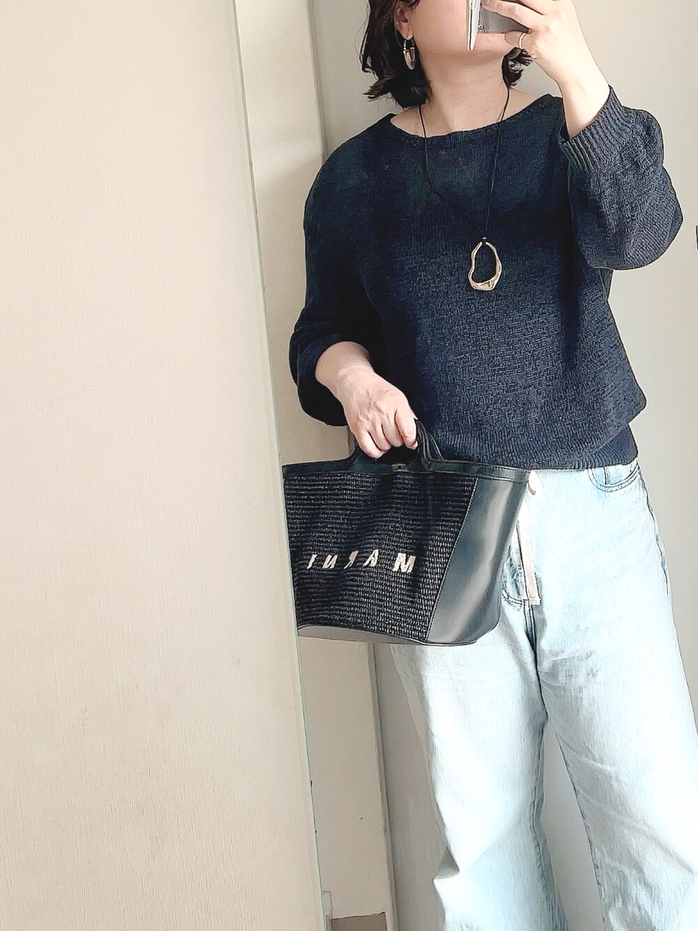 ブルー系のデニムパンツ、ホワイト系のサンダル、ブラック系のハンドバッグを着用したレディースの春コーディネートの2枚目の写真