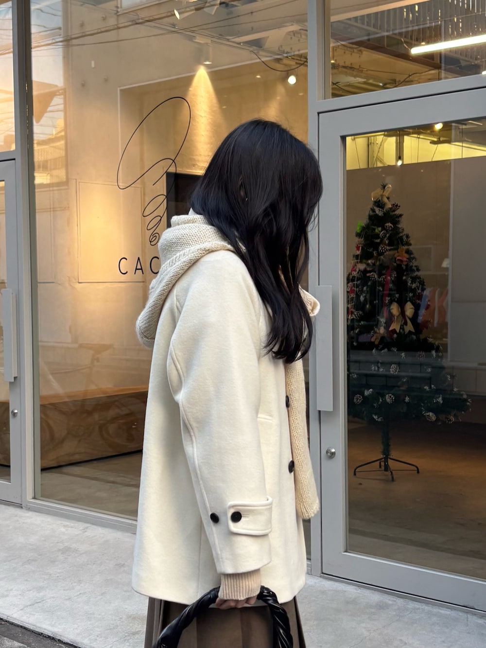 ホワイト系のピーコート、ブラウン系のスカート、ブラック系のハンドバッグを着用したレディースの冬コーディネートの3枚目の写真