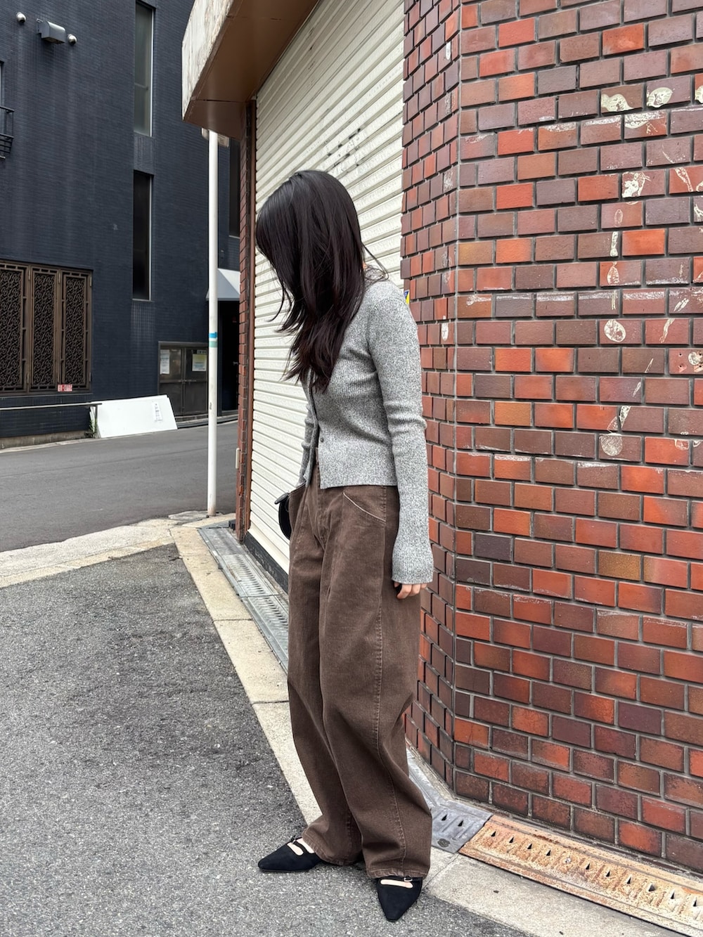 ブラウン系のデニムパンツ、グレー系のニット/セーター、ブラック系のショルダーバッグを着用したレディースの秋コーディネートの2枚目の写真