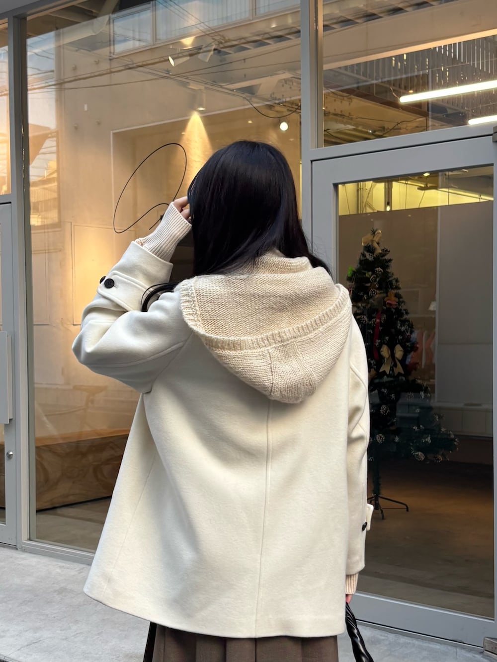 ホワイト系のピーコート、ブラウン系のスカート、ブラック系のハンドバッグを着用したレディースの冬コーディネートの4枚目の写真