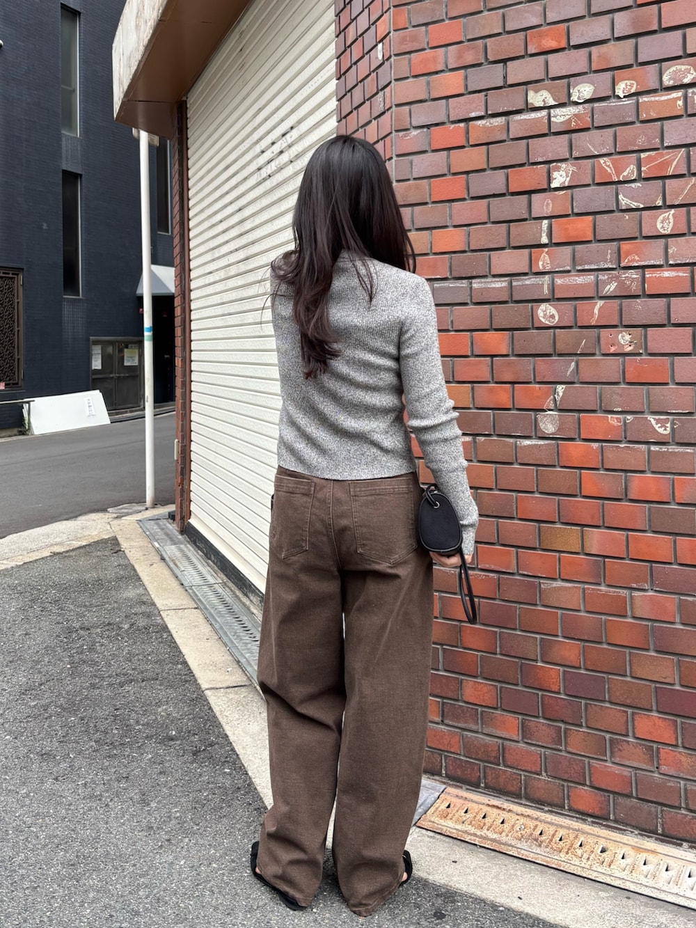 ブラウン系のデニムパンツ、グレー系のニット/セーター、ブラック系のショルダーバッグを着用したレディースの秋コーディネートの3枚目の写真
